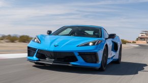 A Rapid Blue 2020 Chevy Corvette travels on a paved surface with an arid landscape, mountains, and a blue sky with wispy clouds in the background