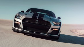 A 2020 Ford Mustang Shelby GT500 with a silver paint job and black racing stripes drives on a racetrack in the desert