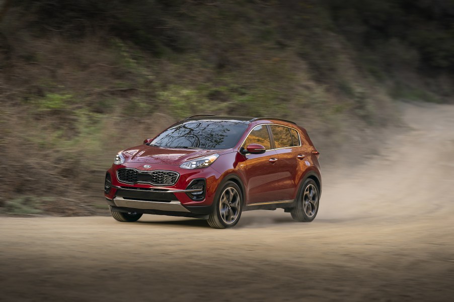 A dark-red 2020 Kia Sportage drives on a dusty dirt road