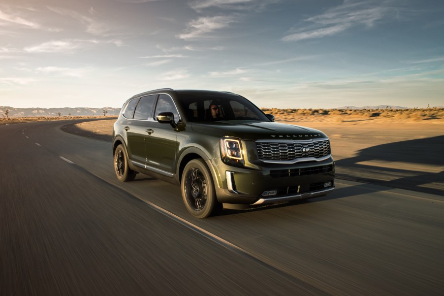 A dark-colored 2020 Kia Telluride drives on a paved road through a desert