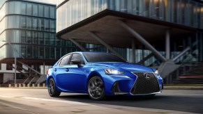 A blue 2020 Lexus IS sedan sits in front of two gray buildings.