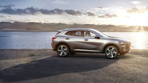 A silver 2021 Buick Envision compact crossover SUV sits next to a lake.