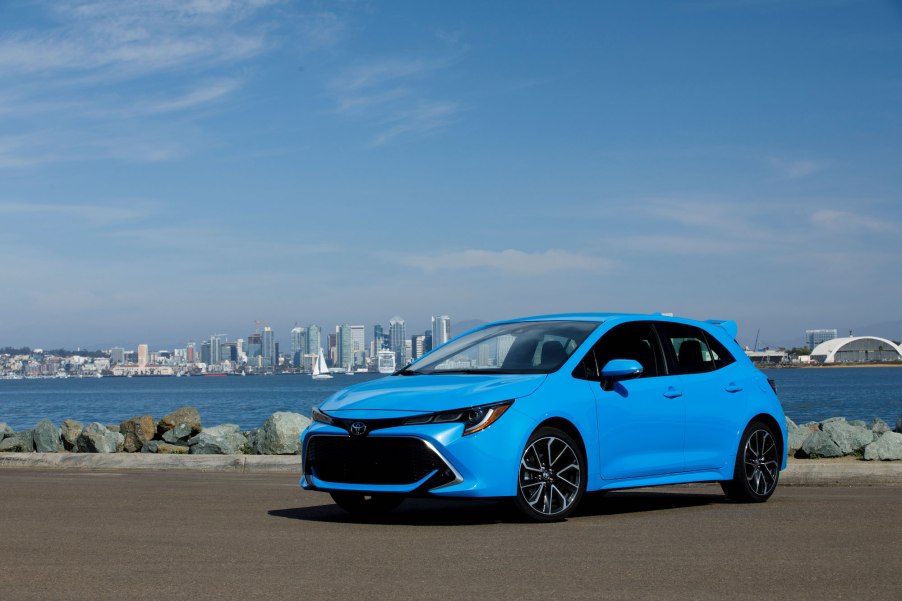 A sky-blue 2021 Toyota Corolla hatchback sits in front of a bay and cityscape