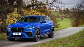 A blue 2021 Jaguar F-Pace SVR driving down a road near a tree