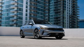 A silver 2021 Kia K5 parked on display with a skyscraper in the background