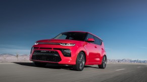 A red 2021 Kia Soul, equipped with standard AEB, drives on a paved surface with a blue sky in the background.