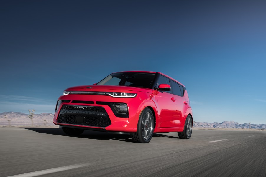 A red 2021 Kia Soul, equipped with standard AEB, drives on a paved surface with a blue sky in the background.