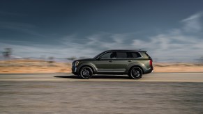 An olive green 2021 Kia Telluride driving down an empty road