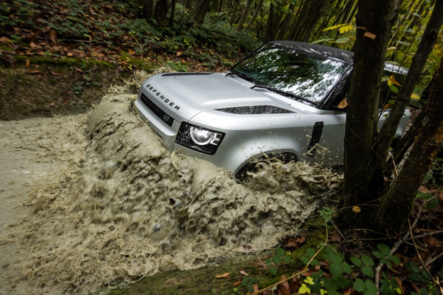 A 2021 Land Rover Defender drives through mud.