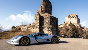 A silver Aspark Owl hypercar near an old fallen stone structure.