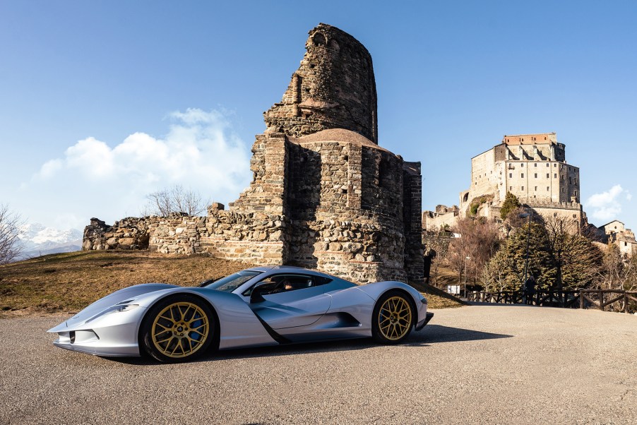 A silver Aspark Owl hypercar near an old fallen stone structure.