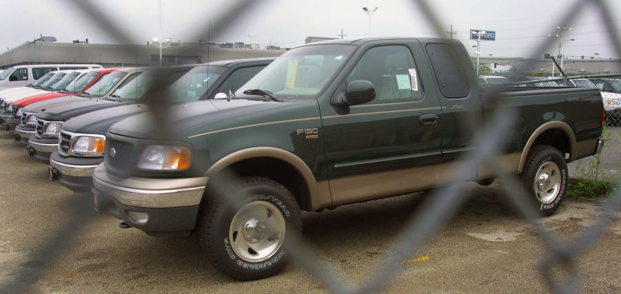 A row of Ford pickup trucks sits behind a gate