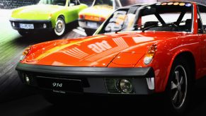 The front of a red Porsche 914 is in the foreground and a poster of another Porsche in the background.