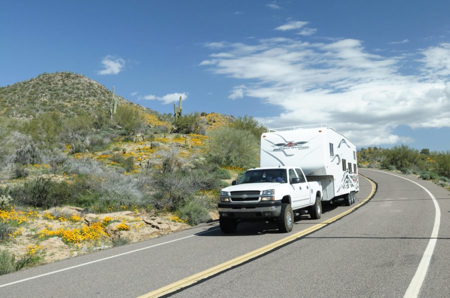 A pickup tows a fifth-wheel RV trailer around a bend in the road.