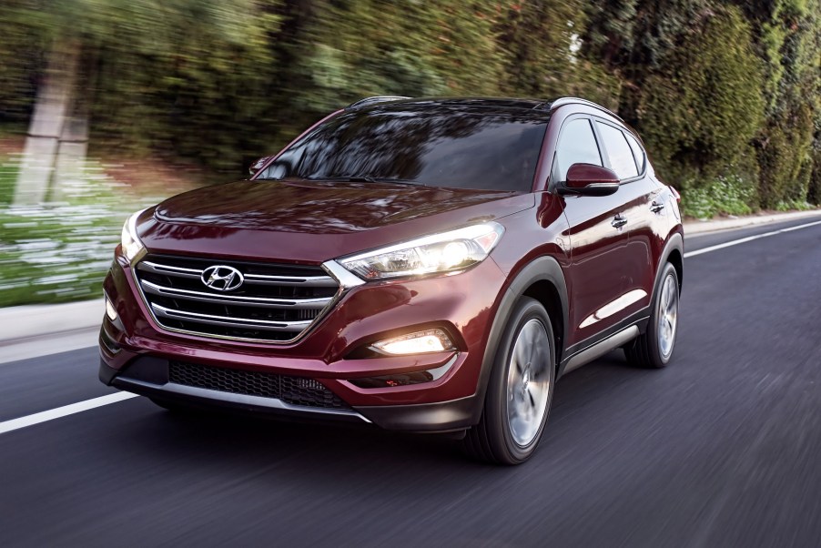 A maroon 2016 Hyundai Tucson travels on a highway lined by foliage