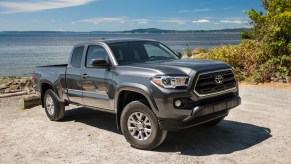 A dark-gray metallic 2016 Toyota Tacoma SR5 parked on gravel next to an ocean