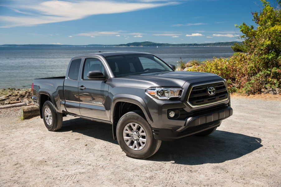 A dark-gray metallic 2016 Toyota Tacoma SR5 parked on gravel next to an ocean