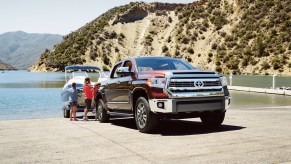 Two children stand next to a maroon 2016 Toyota Tundra towing a boat on a boat ramp overlooking a lake and mountains