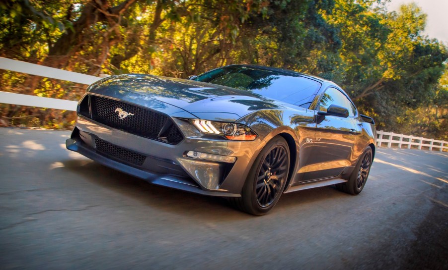 A dark-gray metallic 2020 Ford Mustang on a country road lined by a white wooden fence