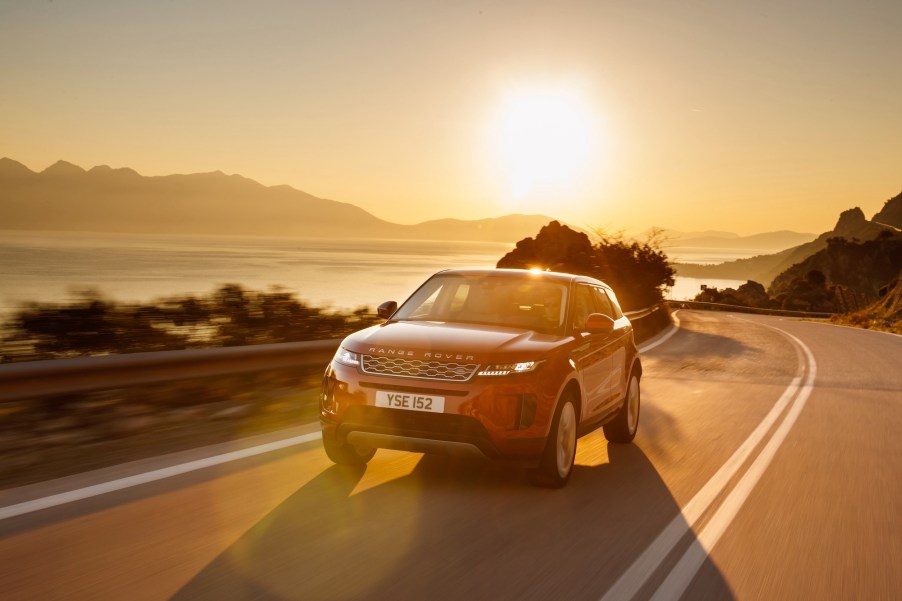 A red 2020 Range Rover Evoque cruises on a paved two-lane road along the water in Greece