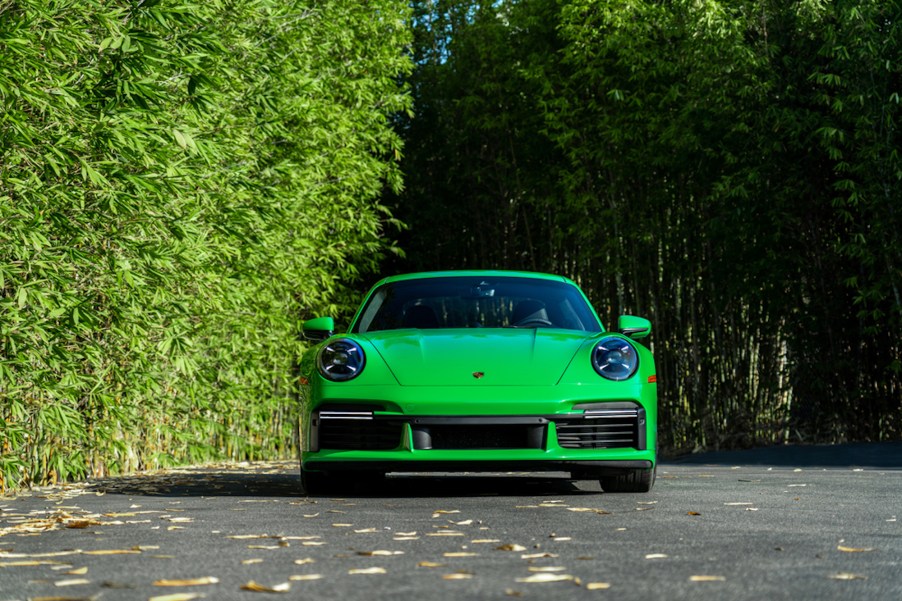 A 2021 Porsche 911 Turbo S in Python Green sits on a paved road next to lush green foliage