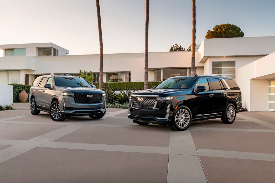 A gray 2021 Cadillac Escalade Sport and a black Premium Luxury parked in front of a large modern white house