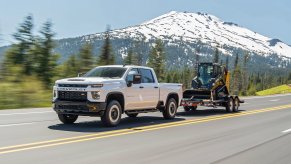 A white 2021 Silverado 2500 HD Custom tows a front-end loader