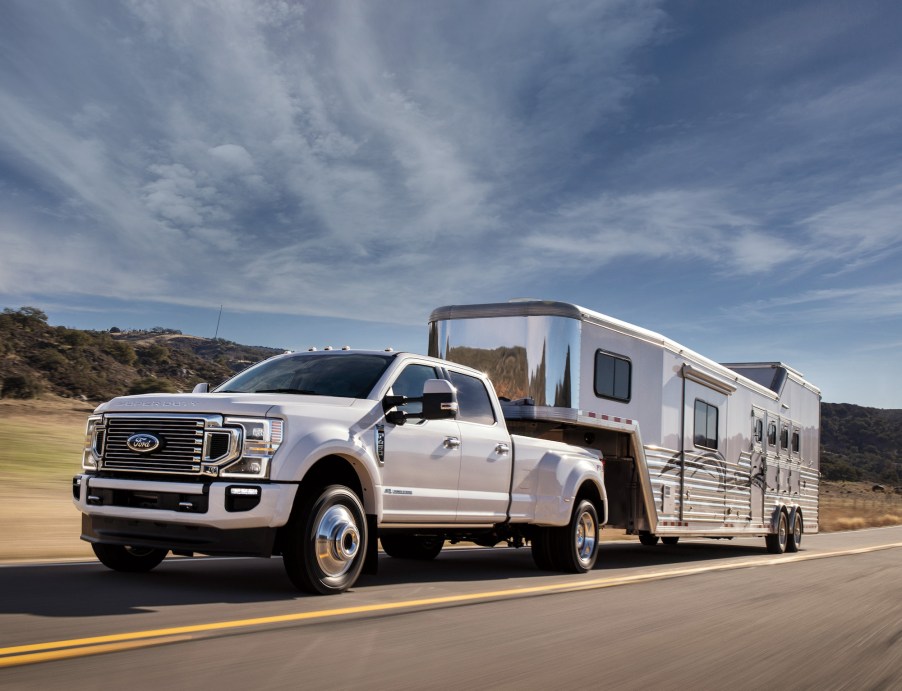 A Ford F-450 Crew Cab 4x4 in Star White Metallic Tinted Clearcoat with FX4 Off-Road Package and available equipment towing a large trailer on the highway