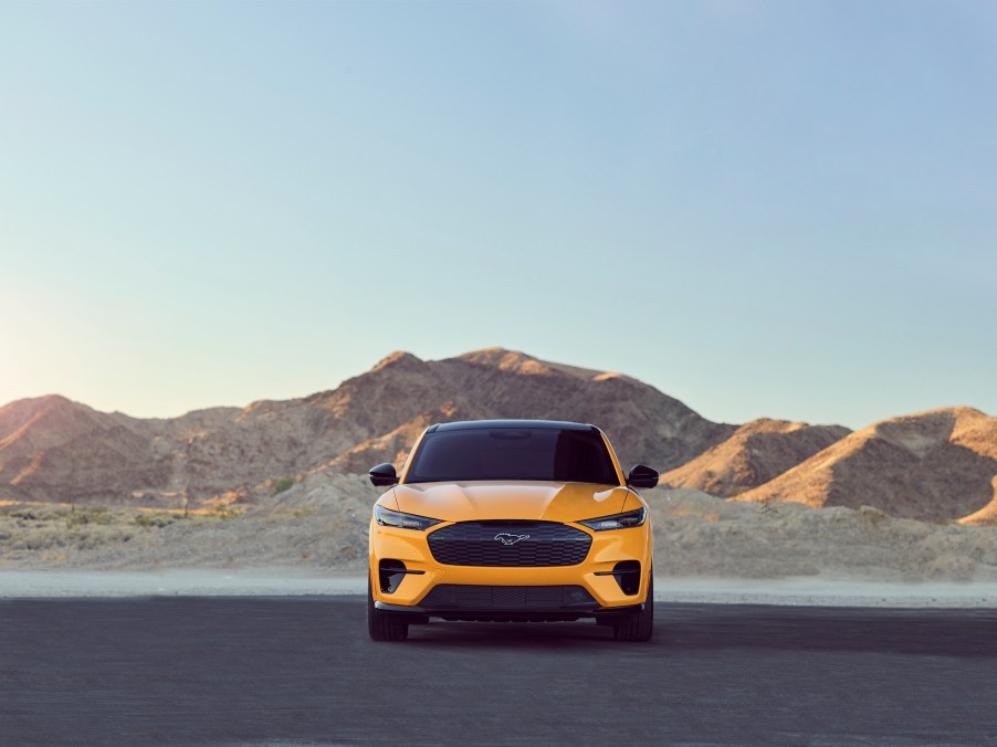 A yellow Ford Mustang Mach-E GT Performance Edition parked on asphalt in front of mountains