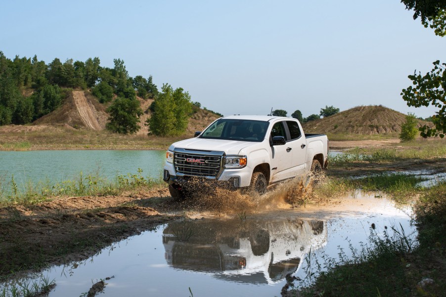 A white 2021 GMC Canyon AT4 Off-Road Performance Edition splashes through muddy water