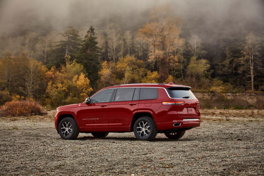 The rear 3/4 view of a red 2021 Jeep Grand Cherokee L Overland by a forest