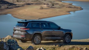 A dark-gray 2021 Jeep Grand Cherokee L Summit Reserve parked overlooking a lake and mountains