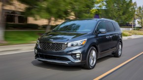 A dark-colored 2021 Kia Sedona travels on a suburban street