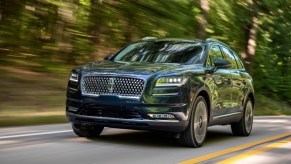 A 2021 Lincoln Nautilus in Flight Blue travels on a two-lane paved road lined by foliage