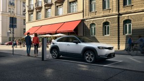 A white Mazda MX-30 charging up while parked next to a building