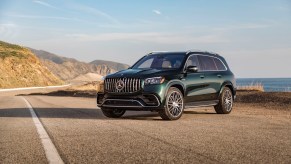 A dark-green 2021 Mercedes-AMG GLS 63 parked on a paved road with blue sky and mountains in the background