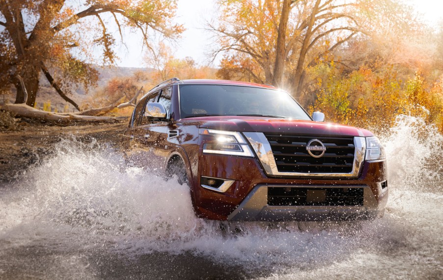 A dark-red 2021 Nissan Armada full-size SUV drives across a creek on a sunny day