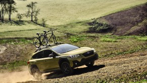 A mustard yellow 2021 Subaru Crosstrek with a bike attached to its roof rack driving down a dirt roat