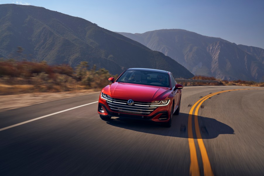 A red 2021 Volkswagen Arteon travels on a two-lane highway through mountains