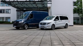 A navy blue Mercedes-Benz eSprinter and a white Mercedes-Benz eVito Tourer parked in a porte cochère