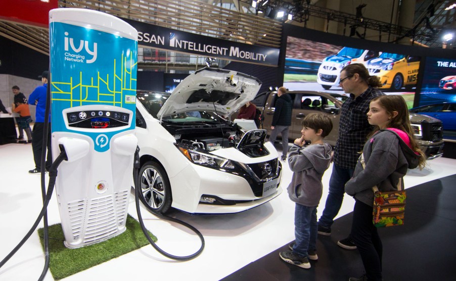 Visitors look at an electric Nissan Leaf Plus vehicle and its charging station during the 2020 Canadian International Autoshow