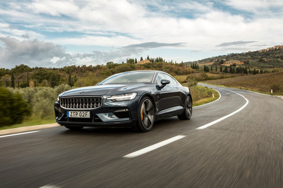 A dark-colored Polestar 1 travels on a two-lane road in the country