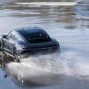 A black Porsche Taycan drifts on wet pavement