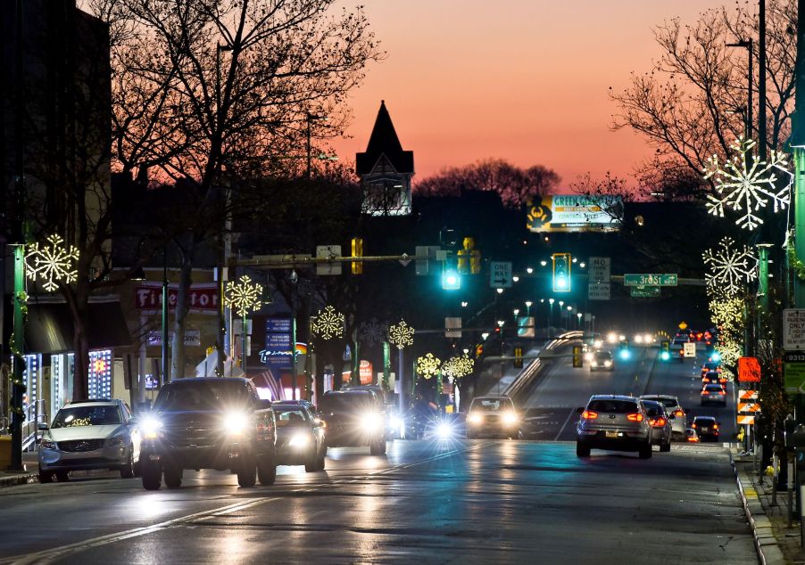 Various cars with their headlights on driving down a city road at dusk