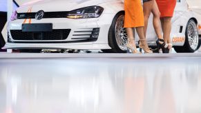 Women with high shoes posing at the Tuning Fair Essen Motor Show for visitors in front of a Golf GTI