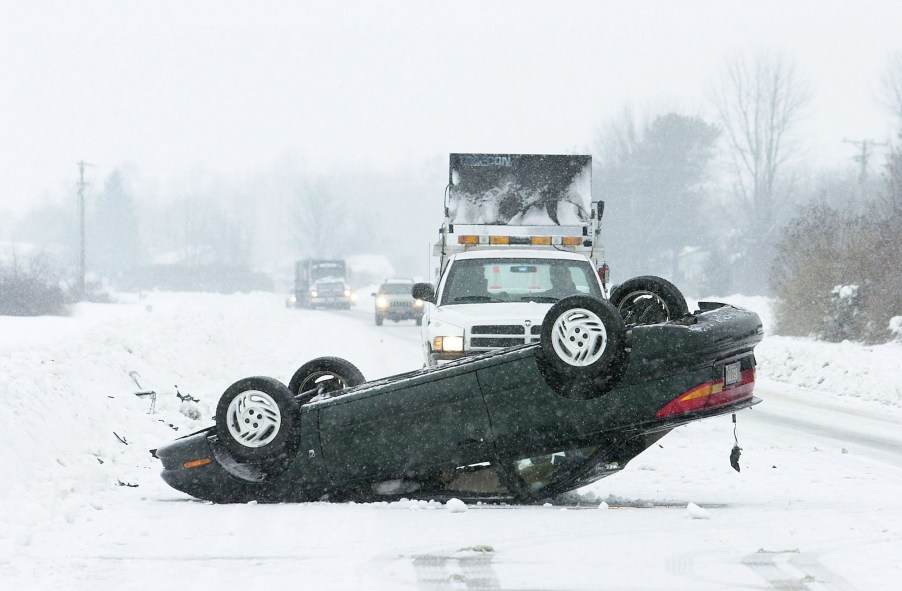 An overturned black car on a snow-covered highway