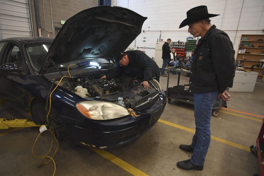 man watches mechanic work on car