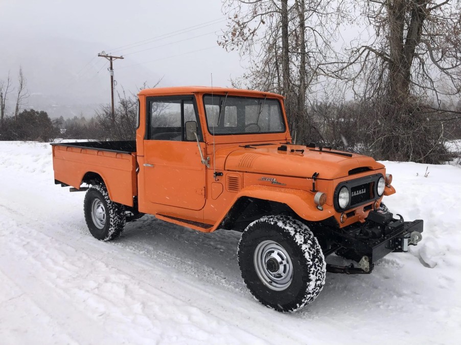 The front 3/4 view of an orange 1964 FJ45 Toyota Land Cruiser pickup in the snow