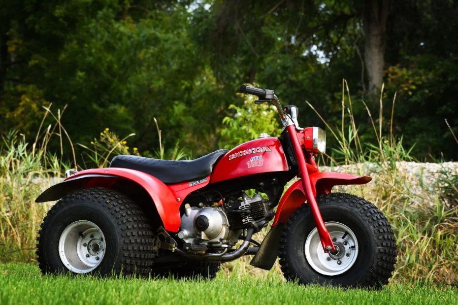 The side view of a red 3-wheeled 1979 Honda ATC 110 in a field