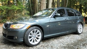 A dark-green 2011 BMW 328i Sports Wagon on a forest gravel path